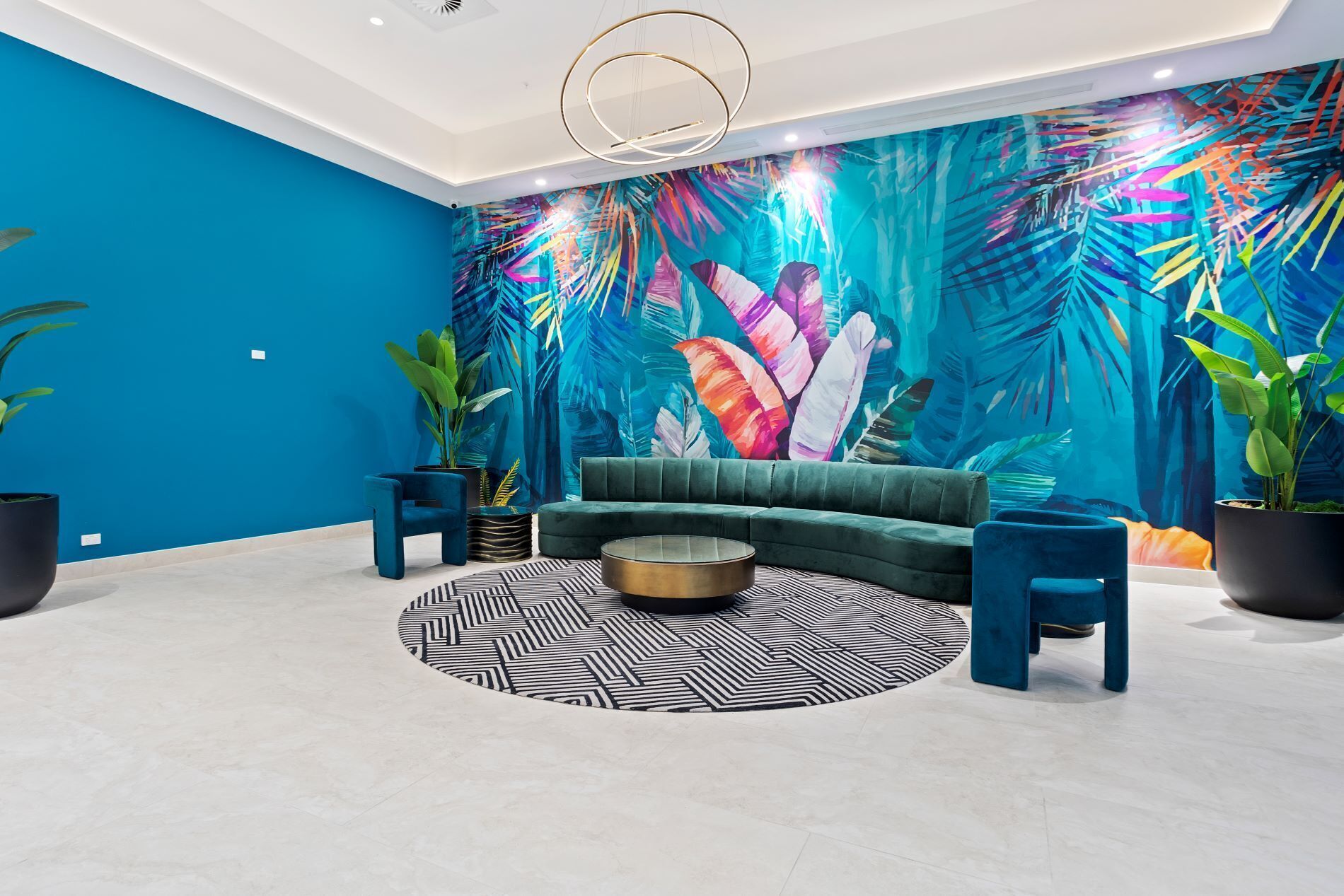 A modern living room with a teal accent wall, a green sofa, a round coffee table, and tropical leaf-patterned wallpaper.