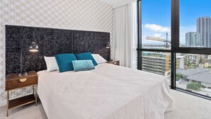 A modern hotel room with a large bed, two bedside tables, and a view of a cityscape through large windows. - Stay Luxe Southport by Coastal Letting Company (Southport)
