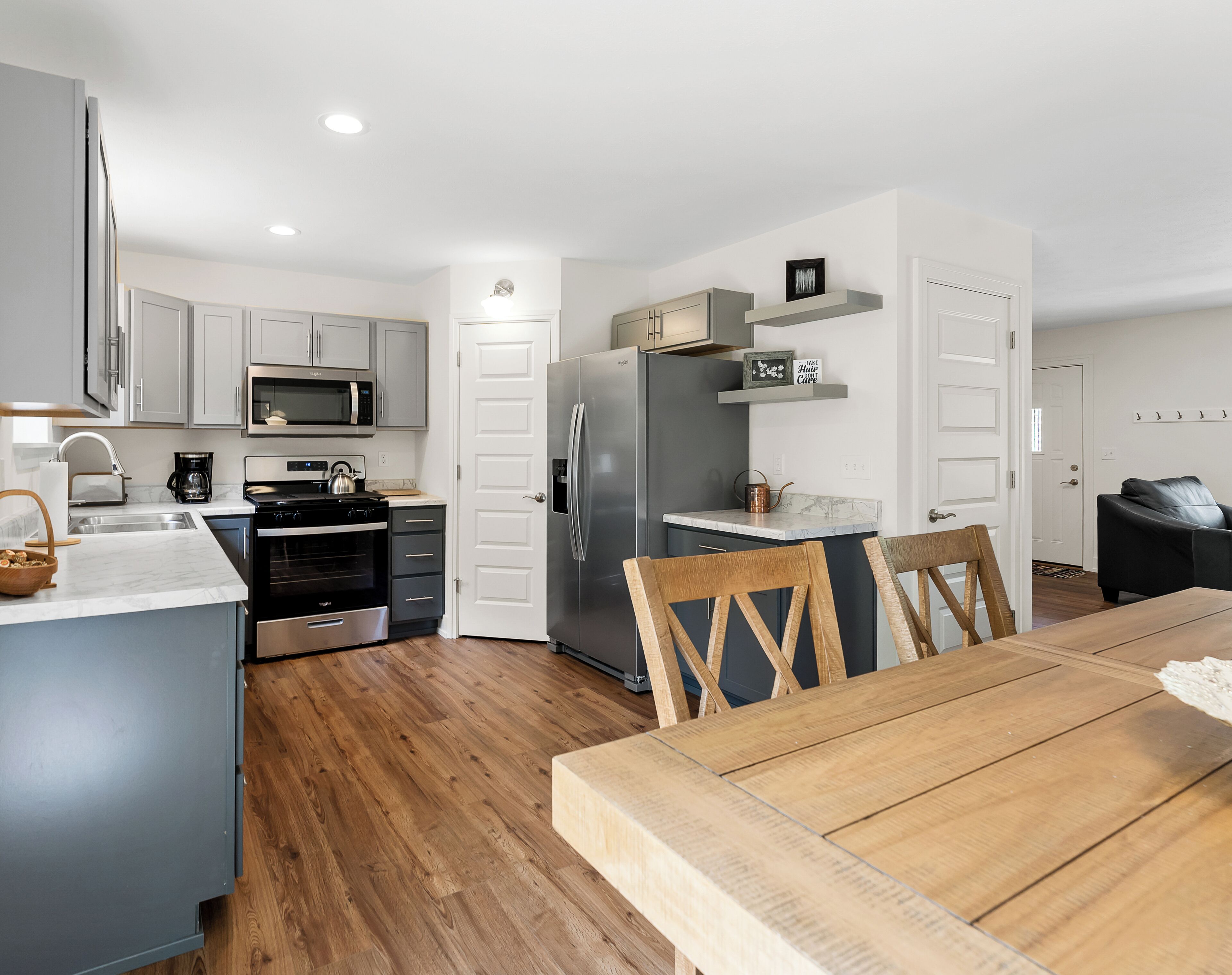 A compact kitchen with modern appliances, a dining area with wooden chairs, and a small living space with a sofa.