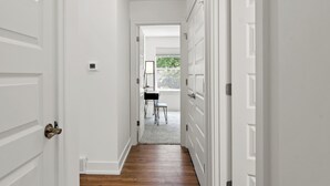 Un pasillo con puertas blancas, suelo de madera y vista a una habitación con una silla y una mesa.