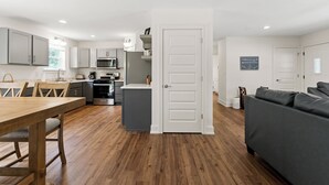 Una cocina moderna con armarios grises, un comedor con mesa de madera y un sofá gris en una sala de estar.