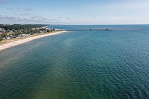 An aerial view of a coastal area with a beach, a pier, and residential buildings. - B30: Pet friendly stay on Lake Michigan | Relax & Unwind (Spring Lake)