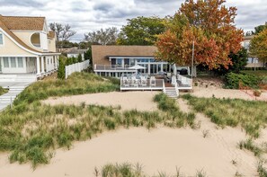 A beachfront property with a patio area, a white fence, and a tree with autumn leaves. - B30: Pet friendly stay on Lake Michigan | Relax & Unwind (Spring Lake)