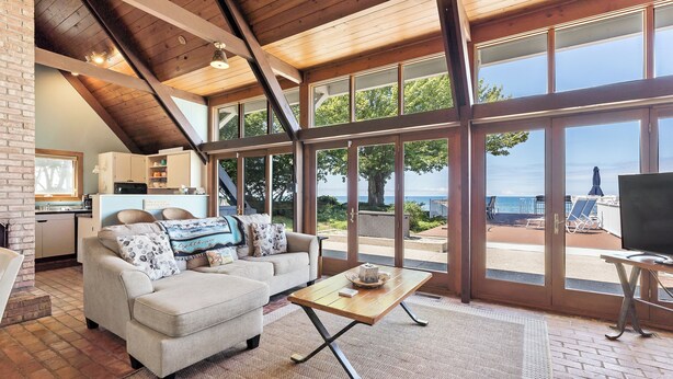 A spacious living area with a large window offering a view of the beach, a cozy sofa, a wooden coffee table, and a television. - B30: Pet friendly stay on Lake Michigan | Relax & Unwind (Spring Lake)