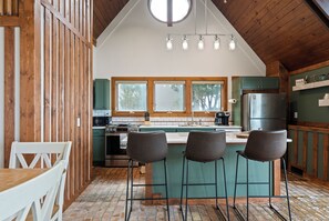A kitchen with a central island, bar stools, a refrigerator, and a window with a view of trees.
