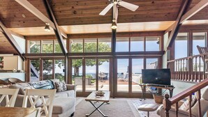 A spacious living area with a large window overlooking a scenic view, a wooden ceiling, and a television on a stand. - B30: Pet friendly stay on Lake Michigan | Relax & Unwind (Spring Lake)