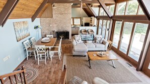 A spacious living area with a fireplace, a dining table with chairs, a sofa with decorative pillows, and large windows offering a view of the outdoors. - B30: Pet friendly stay on Lake Michigan | Relax & Unwind (Spring Lake)