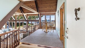 A wooden deck with a view of the sea, a dining area with chairs and a table, and a staircase leading to an upper level. - B30: Pet friendly stay on Lake Michigan | Relax & Unwind (Spring Lake)
