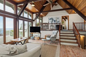 A spacious living area with a large window, a flat-screen TV, a comfortable sofa, and a staircase leading to an upper level.