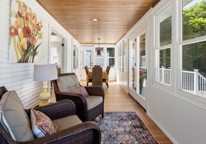 A covered porch with wicker furniture, a dining area, and large windows. - Pier Michigan - seconds away from Lake Michigan and a public access (Grand Haven)