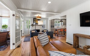 A modern living room with a leather sofa, a dining area, and a kitchen with white paneling and a flat-screen TV. - Pier Michigan - seconds away from Lake Michigan and a public access (Grand Haven)