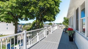 Um deck de madeira com guarda-corpos brancos, um vaso com flores vermelhas e vista para o mar.