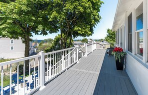Eine Holzterrasse mit weißen Geländern, ein Blumentopf mit roten Blüten und Blick aufs Meer.