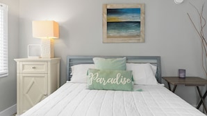 Ein Schlafzimmer mit Bett, Nachttisch mit Lampe, einem kleinen Tisch mit Kerze und einem Bild an der Wand.