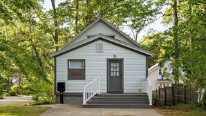 A small, single-story house with a front porch, a mailbox, and a 'HOME' sign on the door. - Captain's Corner | Walk to Beach, Relax by the Lake (Spring Lake)