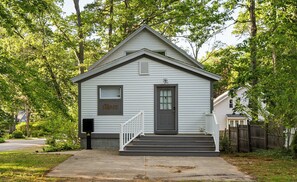 A small, single-story house with a front porch, a mailbox, and a 'HOME' sign on the door. - Captain's Corner | Walk to Beach, Relax by the Lake (Spring Lake)