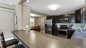 A kitchen with granite countertops, stainless steel appliances, and dark wooden cabinets. - Captain's Corner | Walk to Beach, Relax by the Lake (Spring Lake)