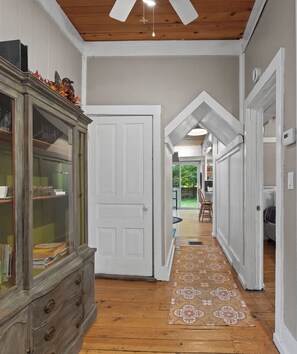 Un couloir avec un plancher en bois, un tapis Ă motifs, une porte blanche et un ventilateur de plafond.