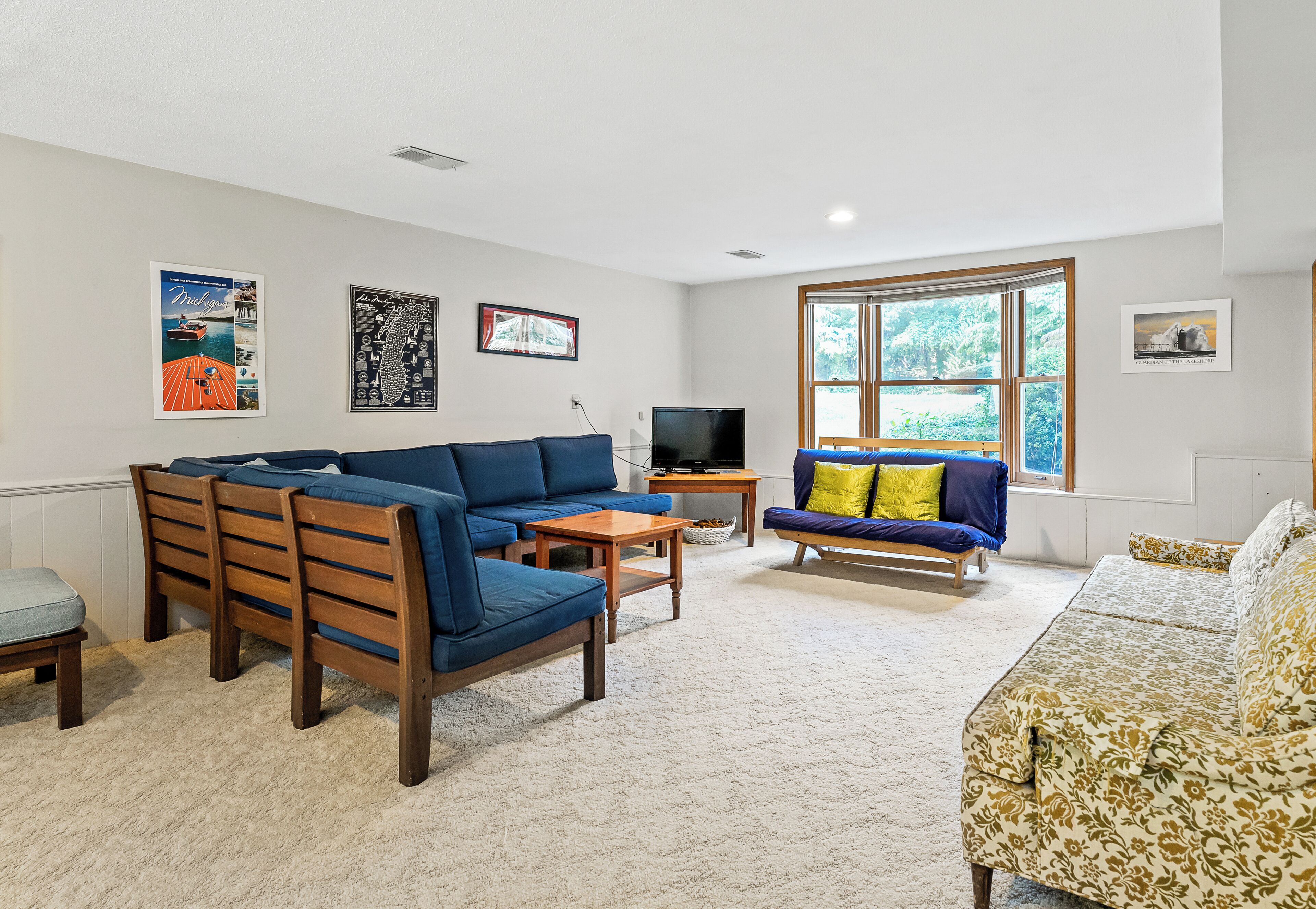A living room with a blue sofa, a patterned sofa, a wooden bench, a small table, and a television.