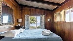 A bedroom with a large bed, a nightstand, a lamp, and a view of the outdoors through a window. - Private Lake Michigan Beach Access (Holland)