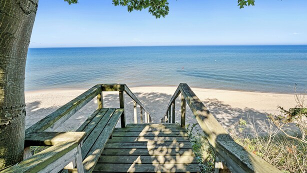 A wooden staircase leading to a beach with clear blue water and a sandy shore. - Private Lake Michigan Beach Access (Holland)