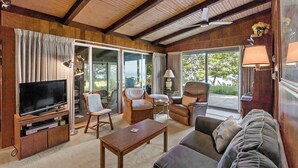 A cozy living room with a television, comfortable seating, a coffee table, and large windows offering a view of the outdoors. - Private Lake Michigan Beach Access (Holland)