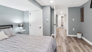 A bedroom with a bed, bedside lamp, and a small white table. - Private pool, close to Lake Michigan Beaches (Muskegon)