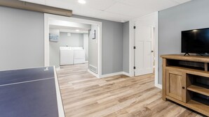A room with a ping pong table, a television on a wooden stand, and a laundry area with a washing machine and dryer. - Private pool, close to Lake Michigan Beaches (Muskegon)