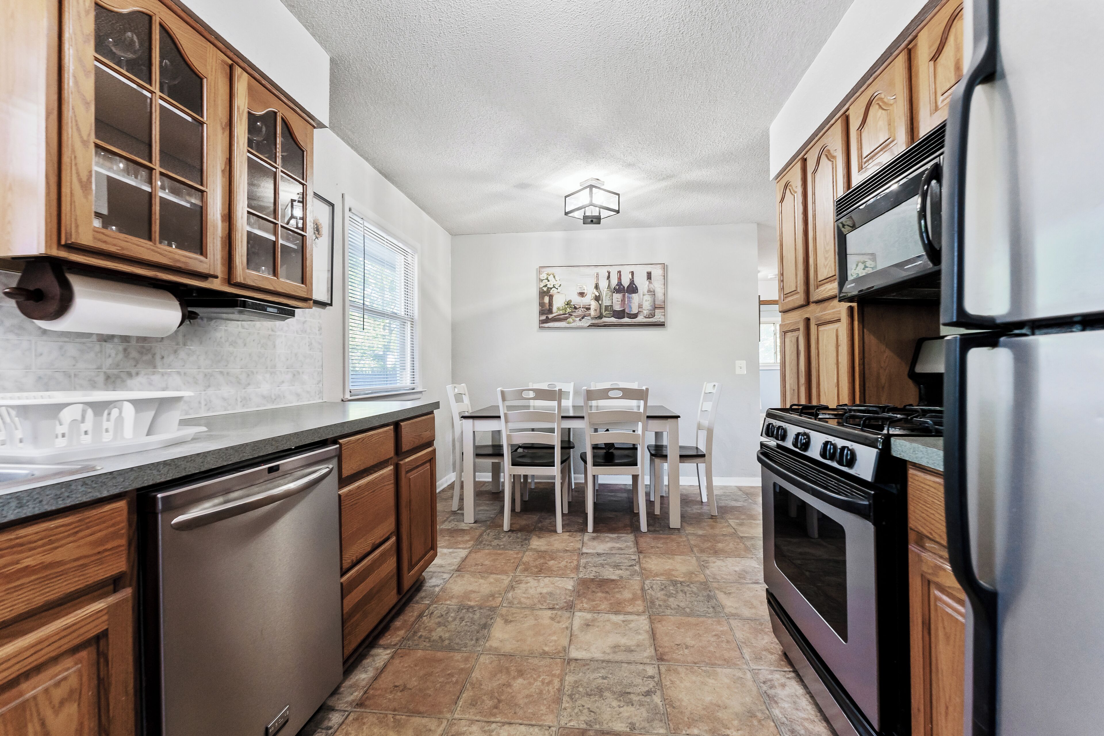 A kitchen with wooden cabinets, a stainless steel refrigerator, a gas stove, and a dining table with chairs.
