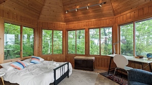 A wooden cabin room with a bed, desk, and large windows.