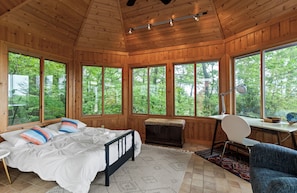 A wooden cabin room with a bed, desk, and large windows.
