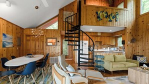 A wooden cabin interior with a dining area, a sofa, a staircase, and a kitchen.