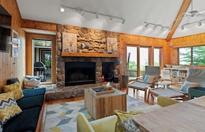 A cozy cabin interior with a stone fireplace, wooden walls, and a comfortable seating area.