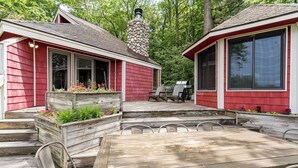 A red wooden house with a deck, a wooden table, and metal chairs.