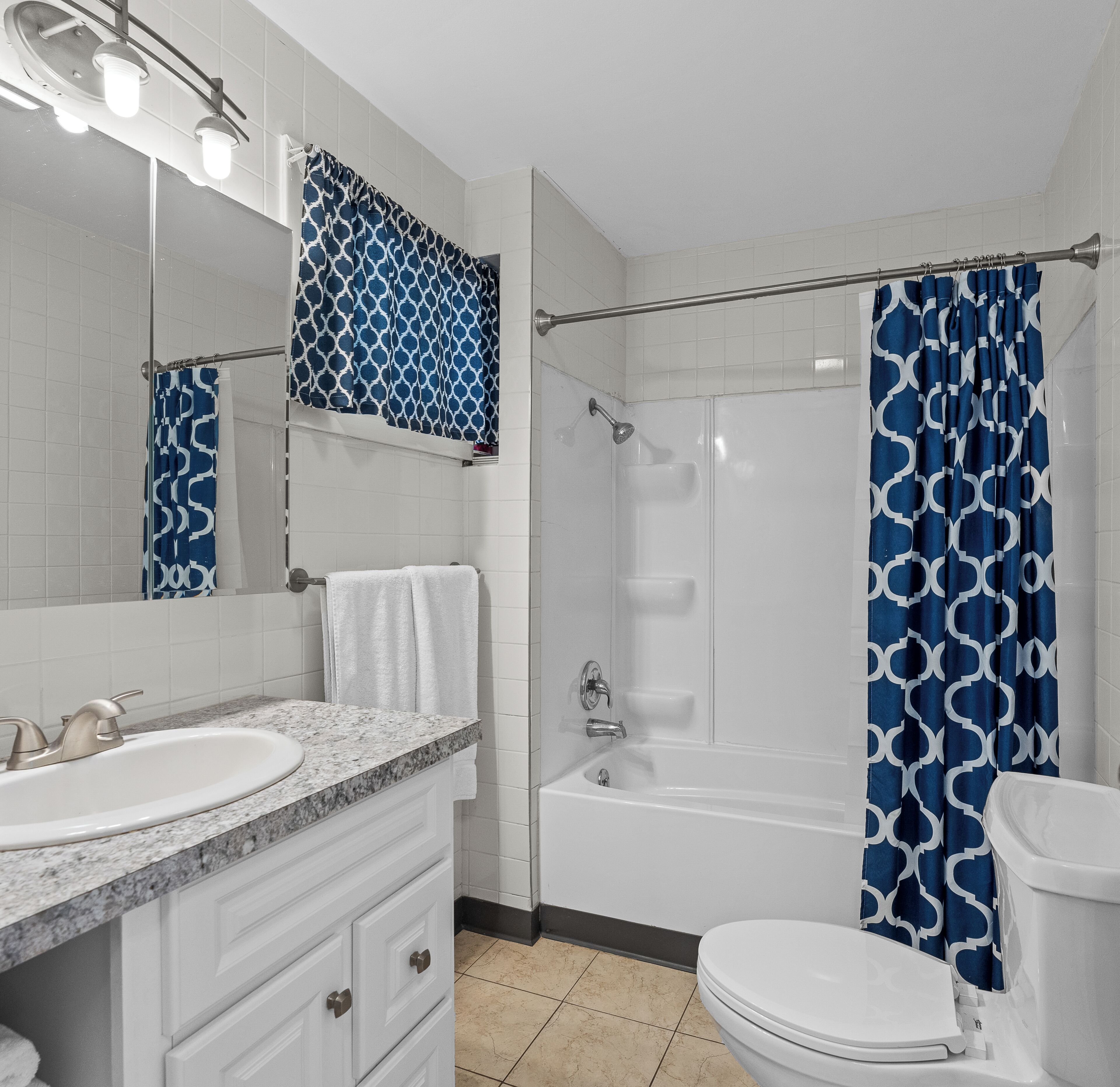 A bathroom with a white sink, vanity, mirror, and toilet. There is a shower area with a blue patterned curtain.