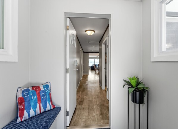 A hallway with a wooden floor, a door leading to a living area, and a potted plant. - Dunes Edge | Steps to Silver Lake & Scenic Dunes (Mears)