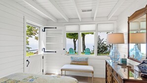 A bedroom with a bed, bench, dresser, and windows with blinds.