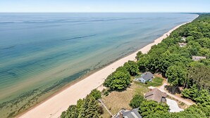 An aerial view of a coastal property with a sandy beach, dense greenery, and a few houses.