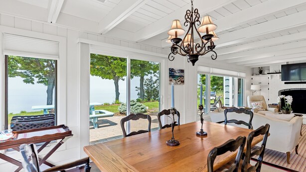 A spacious dining area with a wooden table and chairs, a chandelier, and large windows offering a view of the outdoors.