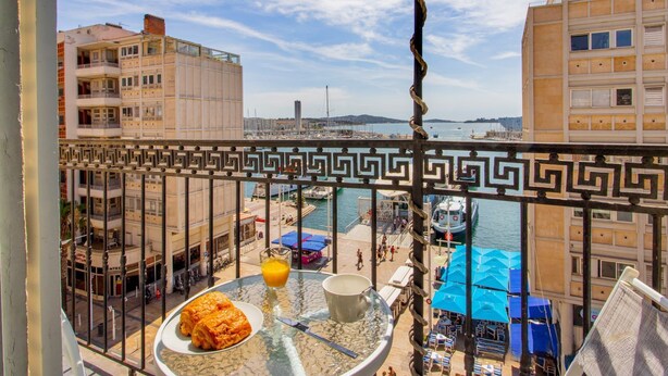 Un balcón con vistas a un puerto deportivo, una mesa de comedor con comida y bebida, y una barandilla con un diseño decorativo.
