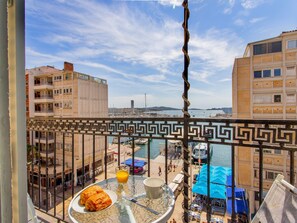Un balcon donnant sur un port de plaisance, une table à manger avec de la nourriture et des boissons, et une balustrade ornée d’un motif décoratif.
