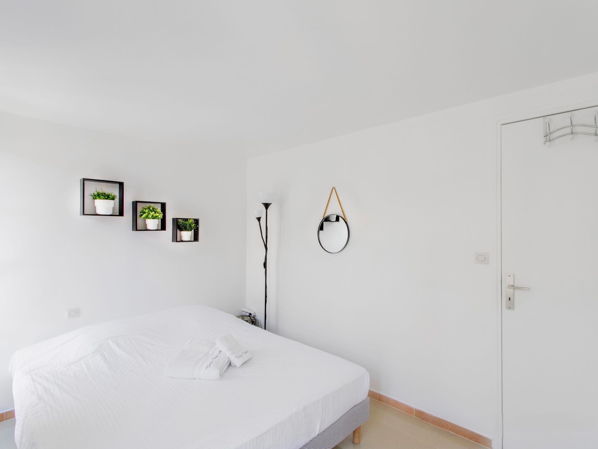 A minimalist bedroom with a bed, a door, and three framed potted plants on the wall.