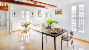 Un salón luminoso con un sofá blanco, una mesa de comedor con sillas y una planta en maceta.