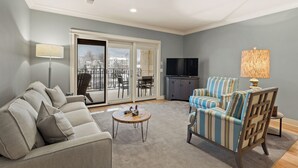 A living room with a sofa, armchair, and a coffee table. There is a TV and a lamp. - Downtown Grand Haven Stay | Spacious 2-Bed in Former Theatre (Grand Haven)