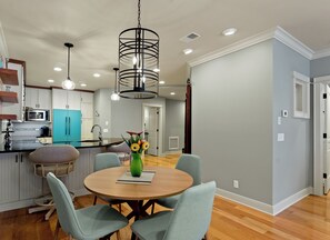 Une cuisine moderne avec des meubles blancs, un réfrigérateur de couleur turquoise et un coin repas comprenant une table ronde en bois et des chaises bleu clair.