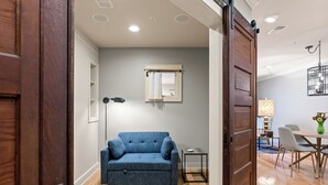 A modern living room with a blue sofa, a small side table, and a dining area with a table and chairs. - Downtown Grand Haven Stay | Spacious 2-Bed in Former Theatre (Grand Haven)