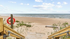 A wooden boardwalk leading to a sandy beach with a lifebuoy on a post.