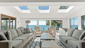 Een moderne woonkamer met een zithoek, een salontafel en uitzicht op de zee door grote ramen.