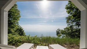 An outdoor seating area with two white lounge chairs and a table, overlooking a body of water and greenery. - Luxury Lakefront Escape | 6 Bedrooms & Pet Friendly (West Olive)