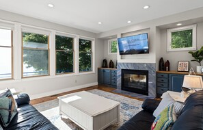 Una sala de estar moderna con chimenea, ventanas amplias, televisor y sofá.